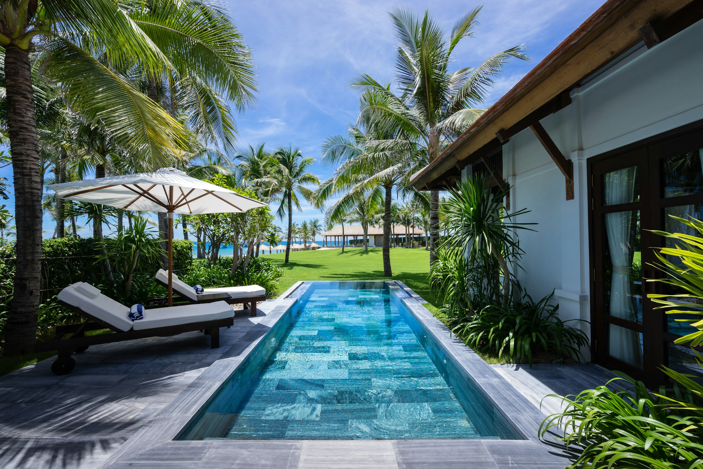 White and brown tropical house with a poolside garden, framed by palm trees
